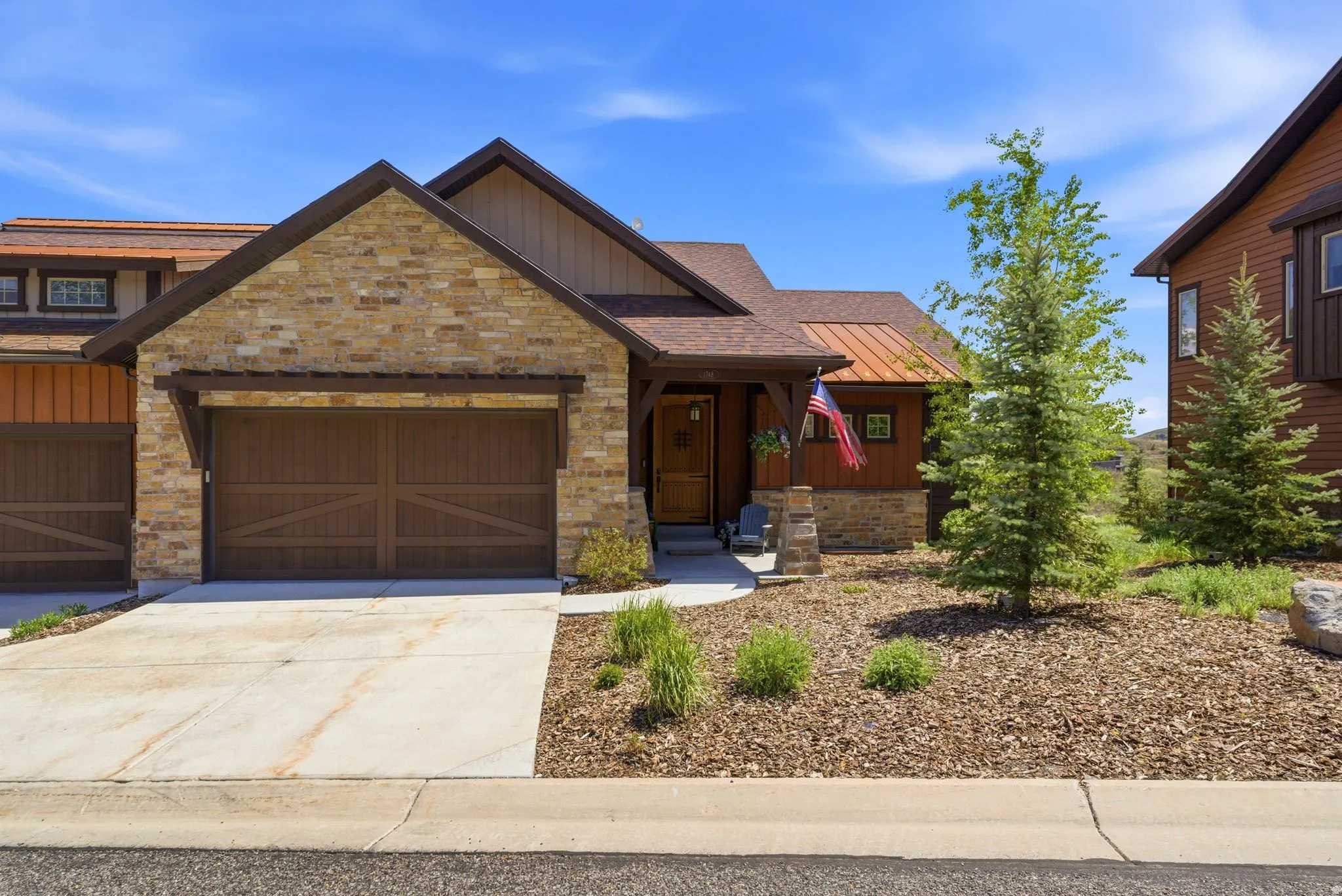 Craftsman-style exterior featuring stone accents, wood siding, a copper-colored metal roof, a two-car garage with wood-finish doors, and a concrete driveway