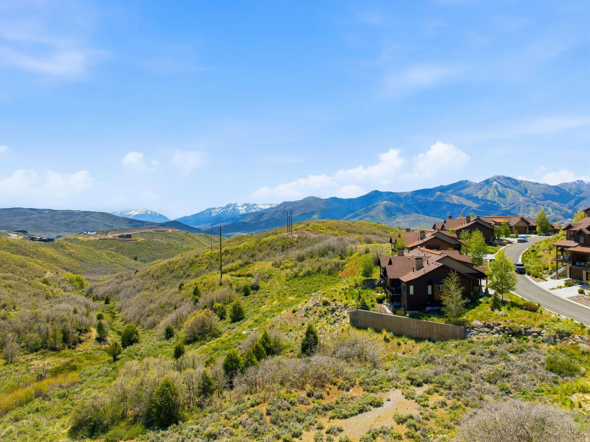 Mountain landscape featuring a residential area with brown-roofed homes, a paved road, and distant snow-capped peaks