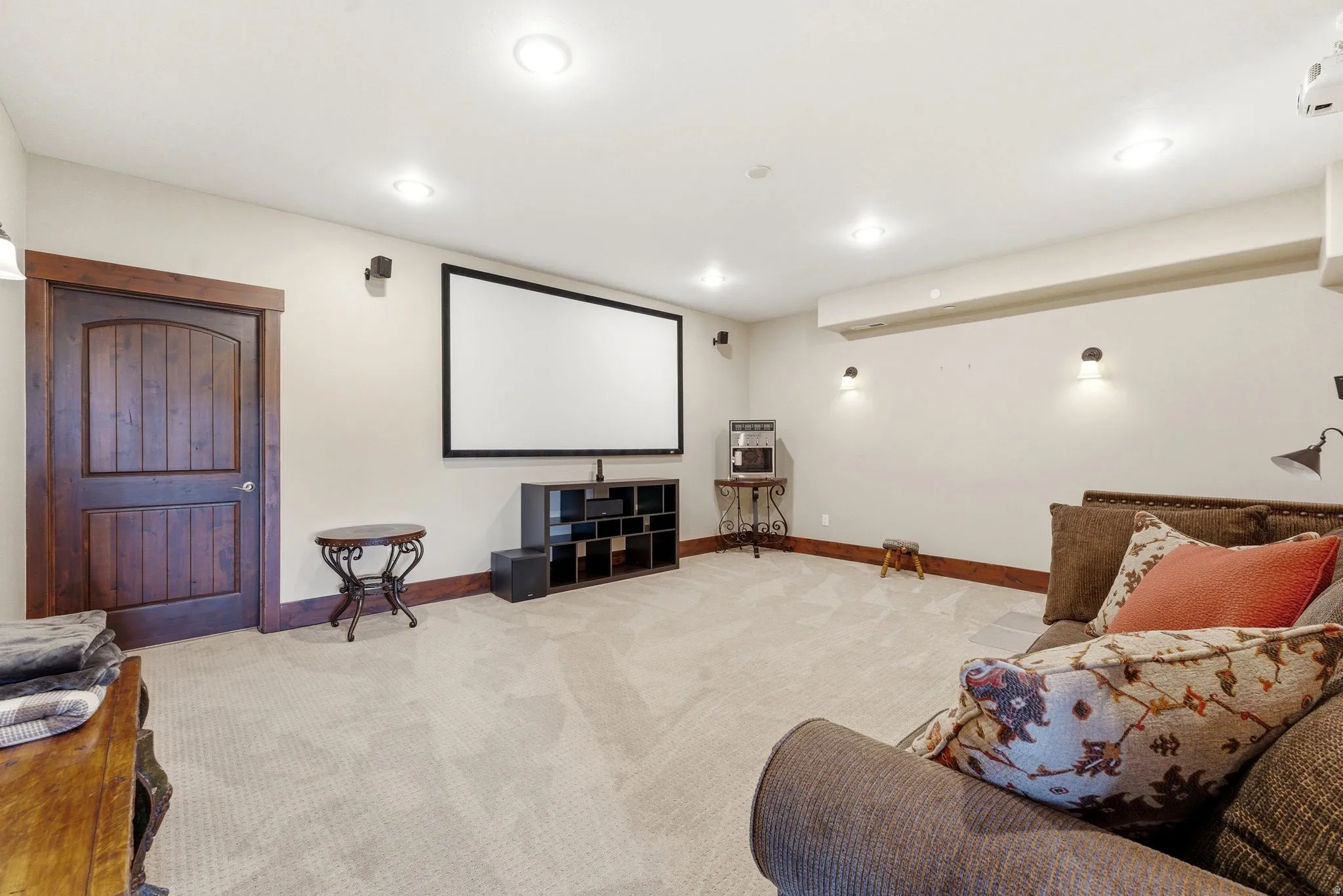 Spacious entertainment area featuring a large projection screen, recessed lighting, and wall-mounted sconces