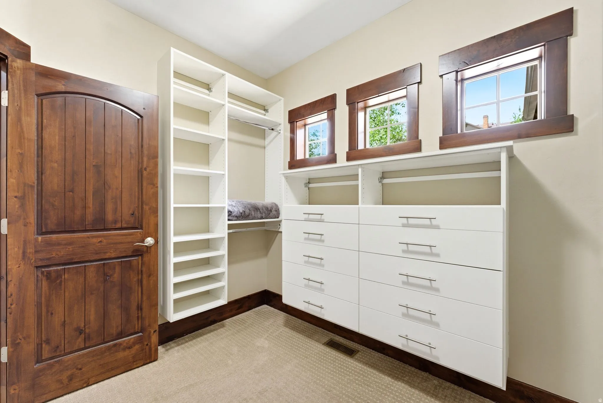 Custom closet system featuring white shelving and drawer units, integrated hanging rods, and three high-set windows with wood trim