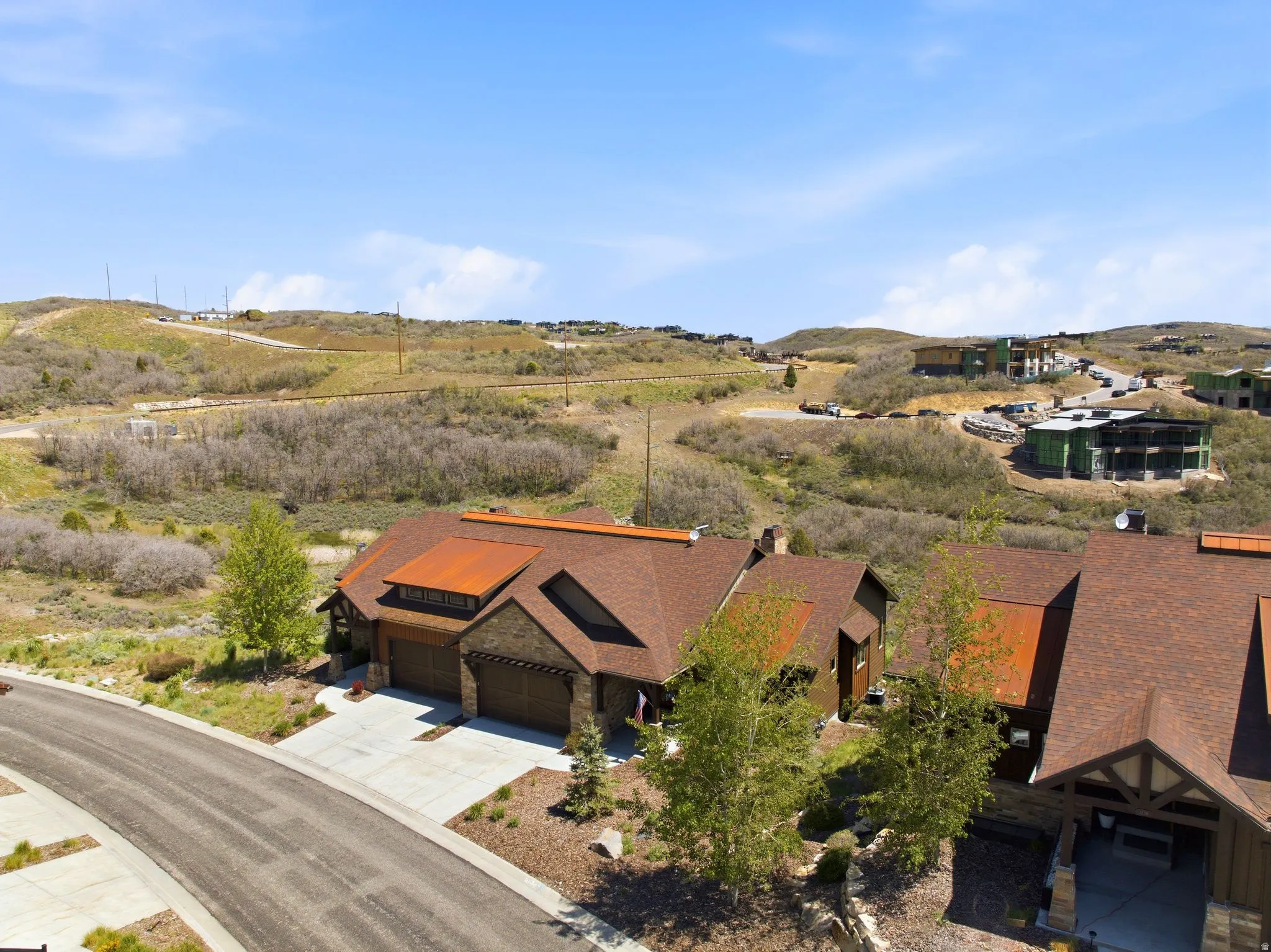 Contemporary residence featuring an integrated two-car garage, stone and wood-panel exterior, and a brown shingled roof with distinctive copper-toned accents