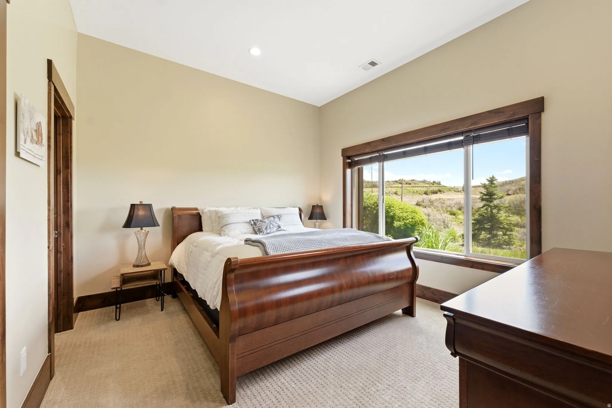 Carpeted room featuring a large window with wood trim, sloped ceiling, recessed lighting, and a solid wood door frame