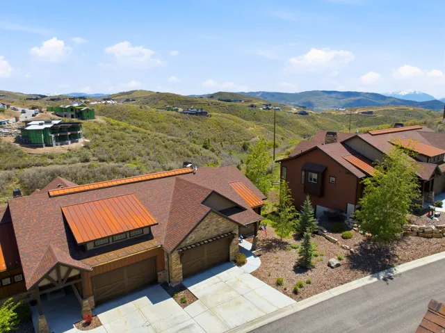 Contemporary mountain-style residence featuring a stone and wood siding facade, a multi-car garage, and a concrete driveway