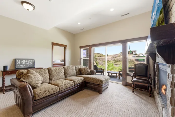 Living area featuring a stone-clad fireplace with wood mantel, sliding glass door access to an exterior patio, recessed ceiling lighting, and a neutral carpet