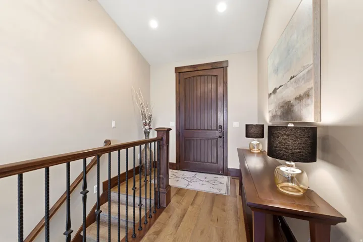 Entryway featuring a solid wood door with vertical paneling, light wood-finish flooring, a dark wood handrail, and wrought iron balusters