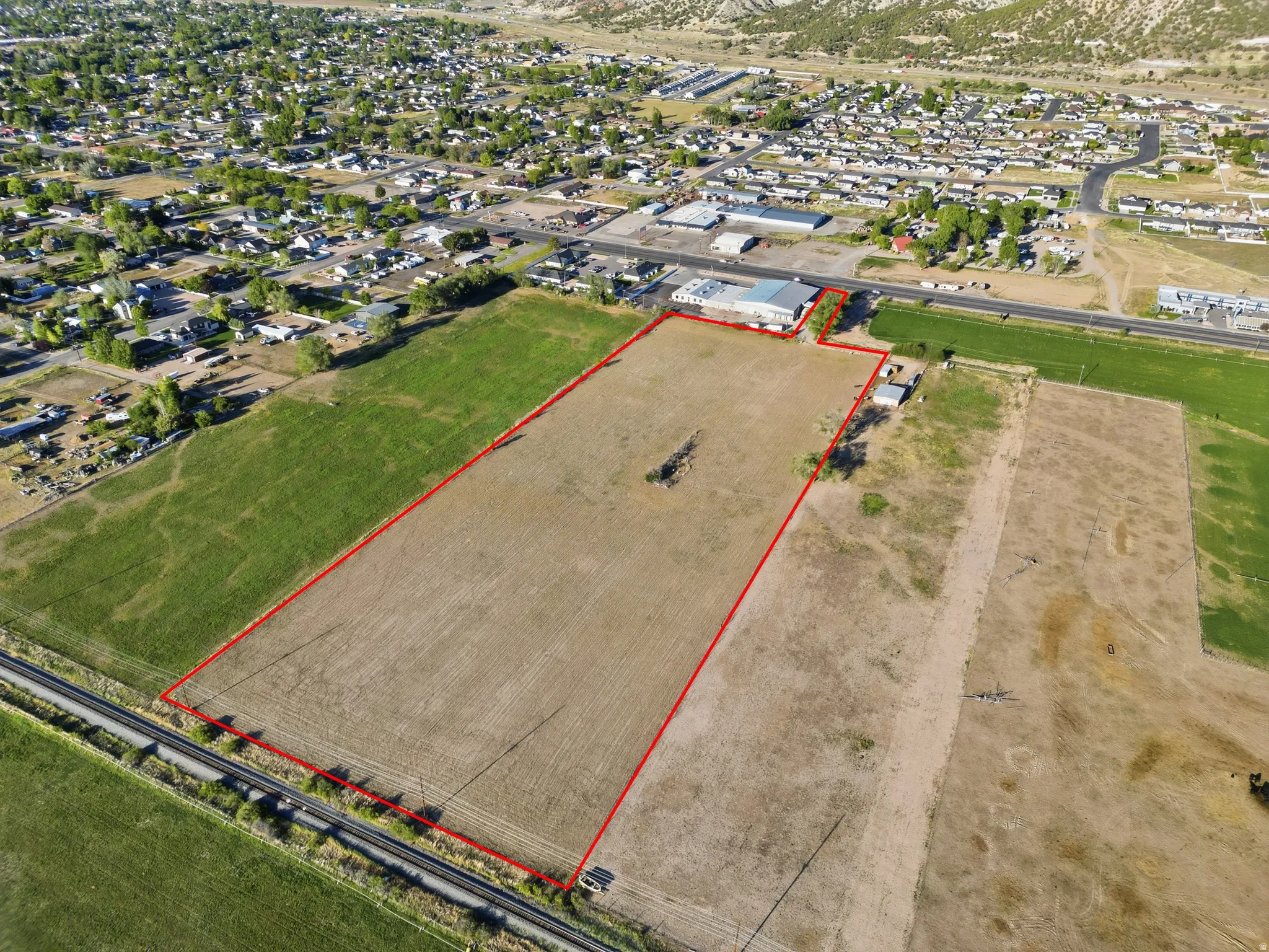 Expansive undeveloped land parcel outlined in red, featuring a rural setting with distant residential areas