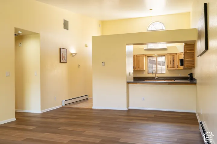 Open concept living area featuring wood-finish flooring, a vaulted ceiling, and a pass-through kitchen with wood cabinetry, a stainless steel sink, and a breakfast bar