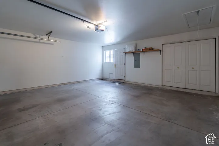 Spacious garage featuring a concrete floor, built-in storage closet, utility access panel, window, and overhead lighting