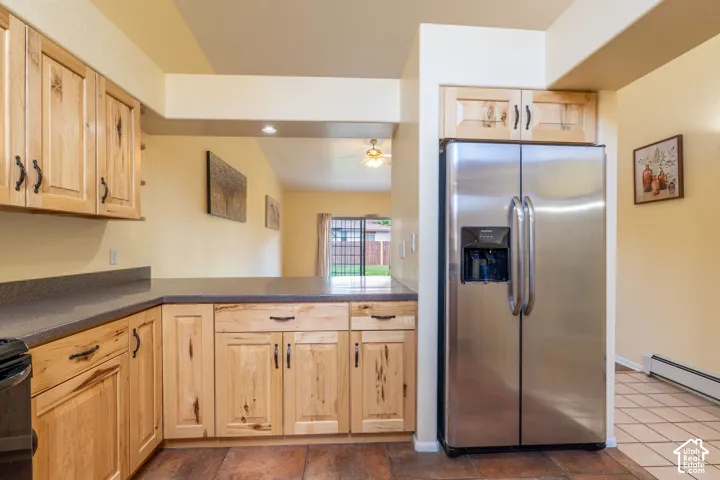 Kitchen with light wood cabinetry, dark countertops, and stainless steel side-by-side refrigerator