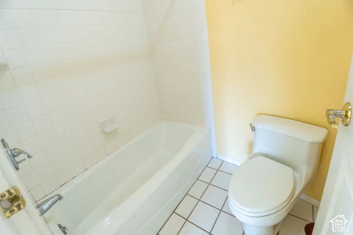 Bathroom featuring a white porcelain bathtub with chrome fixtures, white tile surround, and a white toilet