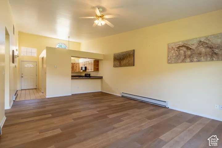 Spacious living area featuring wood-finish flooring, vaulted ceilings, and a ceiling fan with integrated lighting