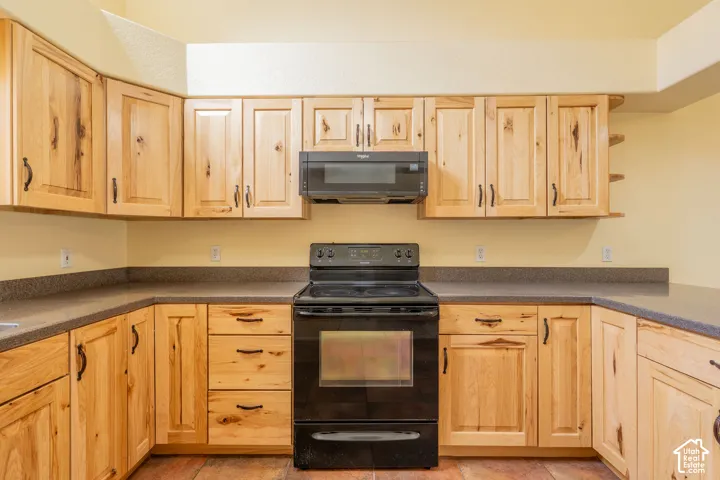 U-shaped kitchen featuring light wood cabinetry with dark hardware, dark stone-finish countertops, and a black built-in oven with an overhead microwave