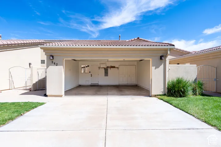 Open carport entrance featuring a concrete driveway, stucco exterior, and red tile roof