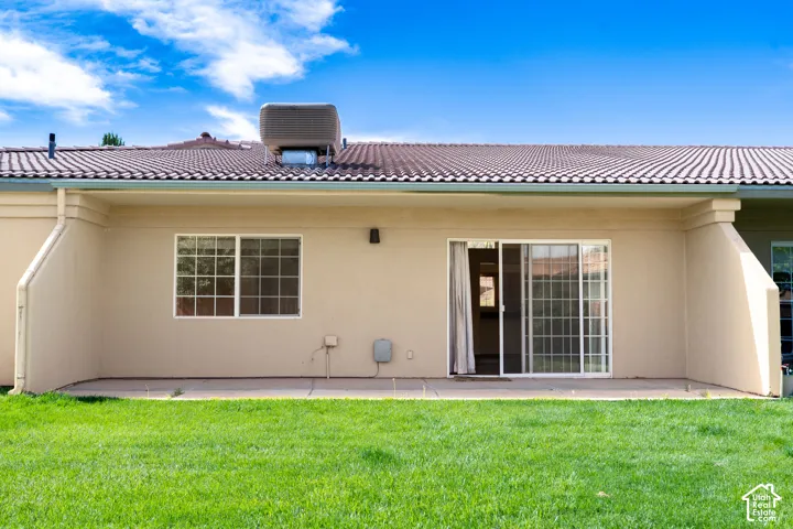 Rear exterior featuring a sliding glass door, a window with grilles, a tile roof, a rain gutter system, and a concrete patio