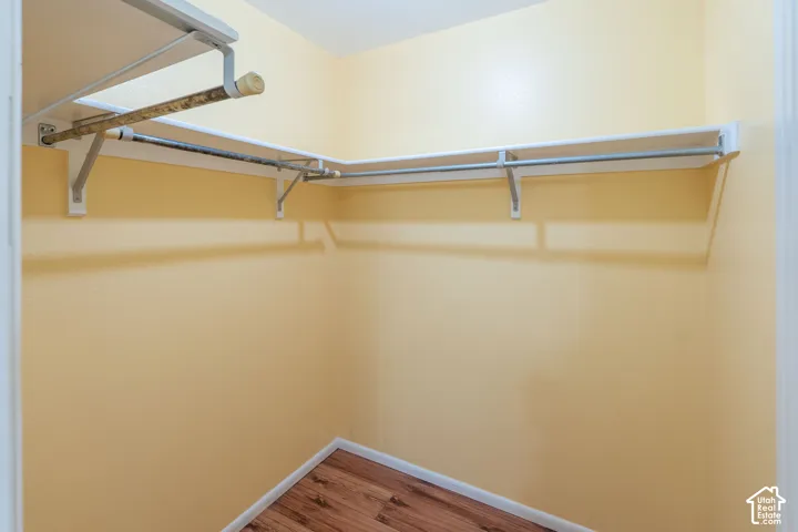 Walk-in closet with warm-toned walls, built-in shelving, and wood-finish flooring