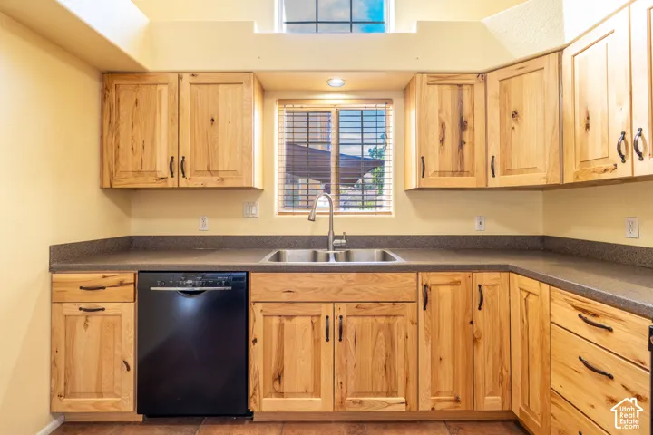 Kitchen featuring light wood cabinetry, dark countertops, a double basin stainless steel sink with a gooseneck faucet, and a built-in black dishwasher