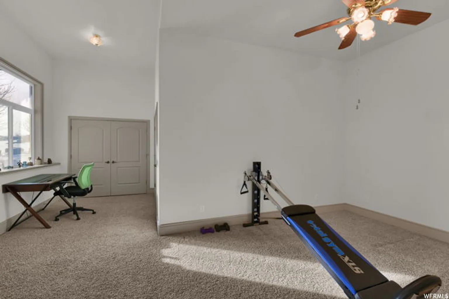 Carpeted interior space featuring a large window, double doors, a flush-mount ceiling light, and a ceiling fan with integrated lighting