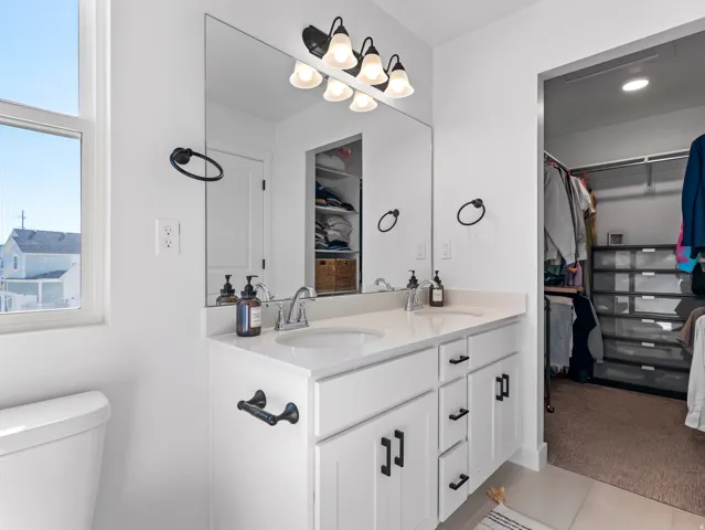 Bright bathroom featuring a double vanity with white cabinetry, light-colored countertops, and two undermount sinks