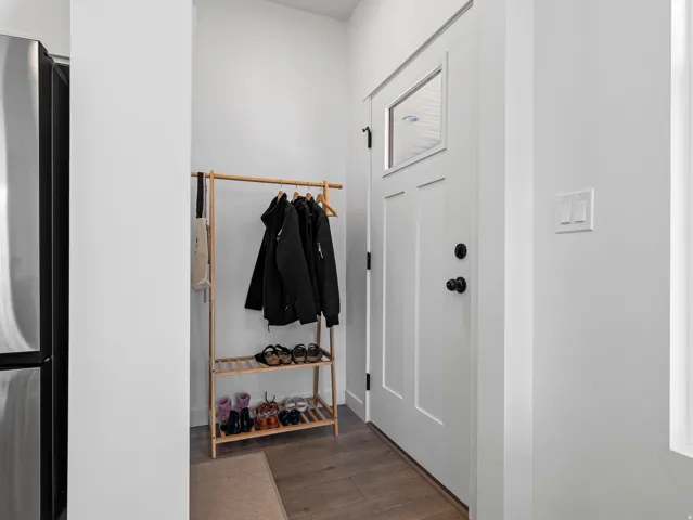 White entry door with a rectangular window pane and matte black hardware, accompanied by wood-finish flooring
