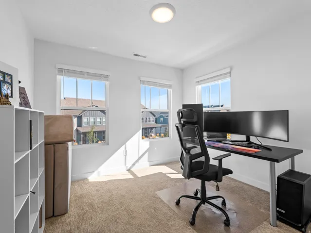 Bright room featuring three windows with white blinds, carpet flooring, a ceiling-mounted light fixture, and white wall paint