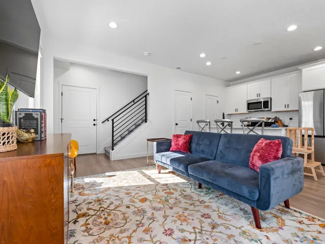 Open-concept living area featuring wood-finish flooring, recessed lighting, and a modern staircase with a black metal railing