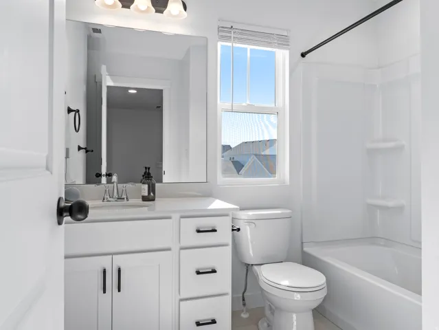 Bathroom featuring a white vanity with black hardware, a rectangular mirror, a bathtub with an integrated shower, and a single window