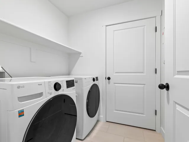 Dedicated laundry area featuring white walls, open shelving, and light-toned tile flooring