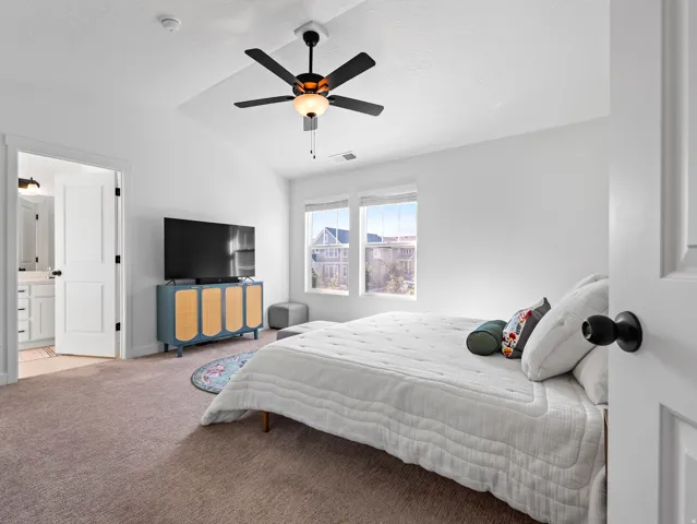 Bright bedroom with vaulted ceilings and a ceiling fan, featuring plush carpeting and two windows