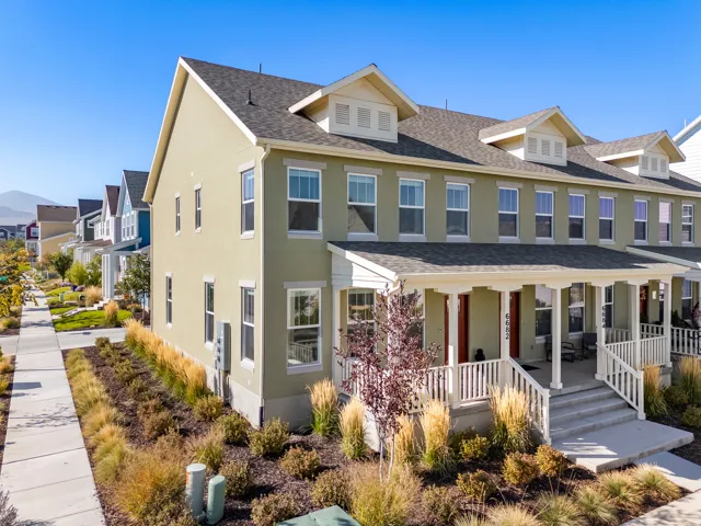 Multi-story property featuring a covered front porch with white railings, a stucco exterior, multiple dormer windows, and a paved walkway