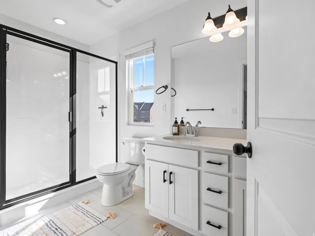 Bathroom with white square floor tiles and a shower featuring a black-framed glass enclosure