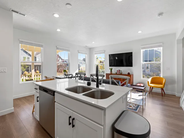 Kitchen island featuring a double basin sink, stainless steel dishwasher, and white cabinetry with black hardware