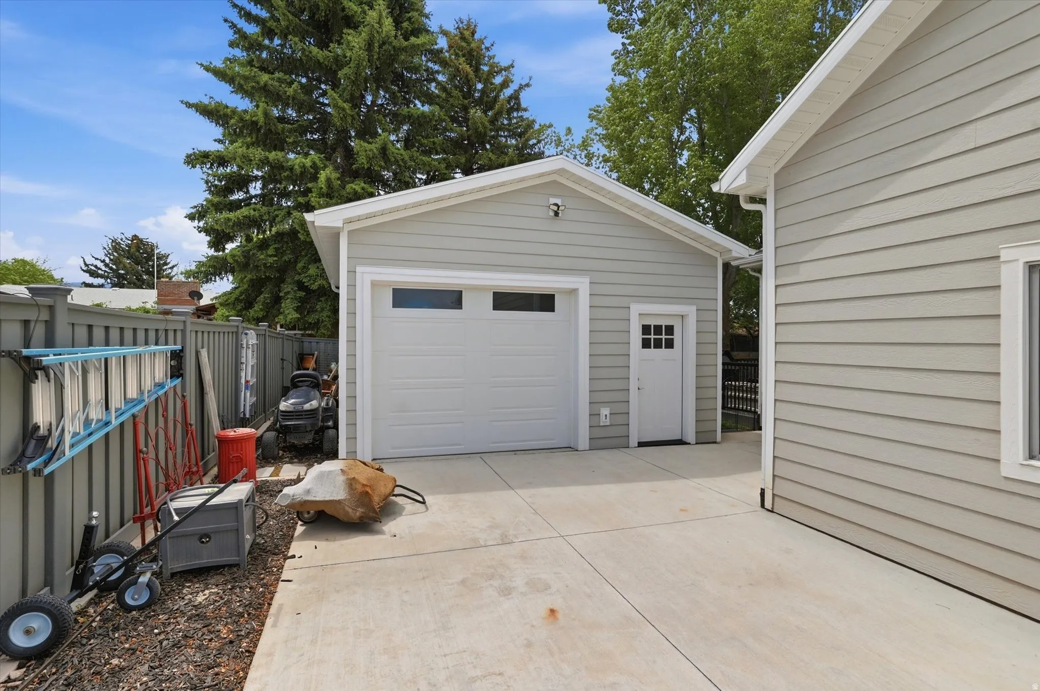 Detached single-car garage featuring light gray siding, a white garage door with upper windows, and a side entry door with lites
