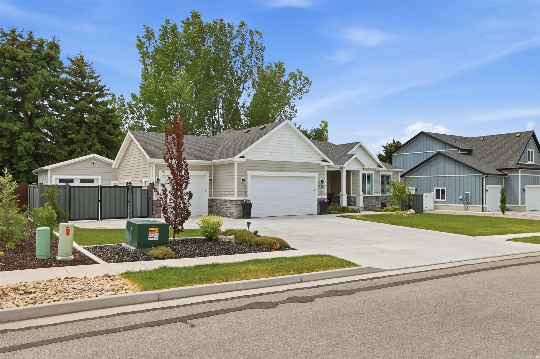 Contemporary ranch-style residence featuring light gray siding, stone accents, a two-car garage, and a concrete driveway