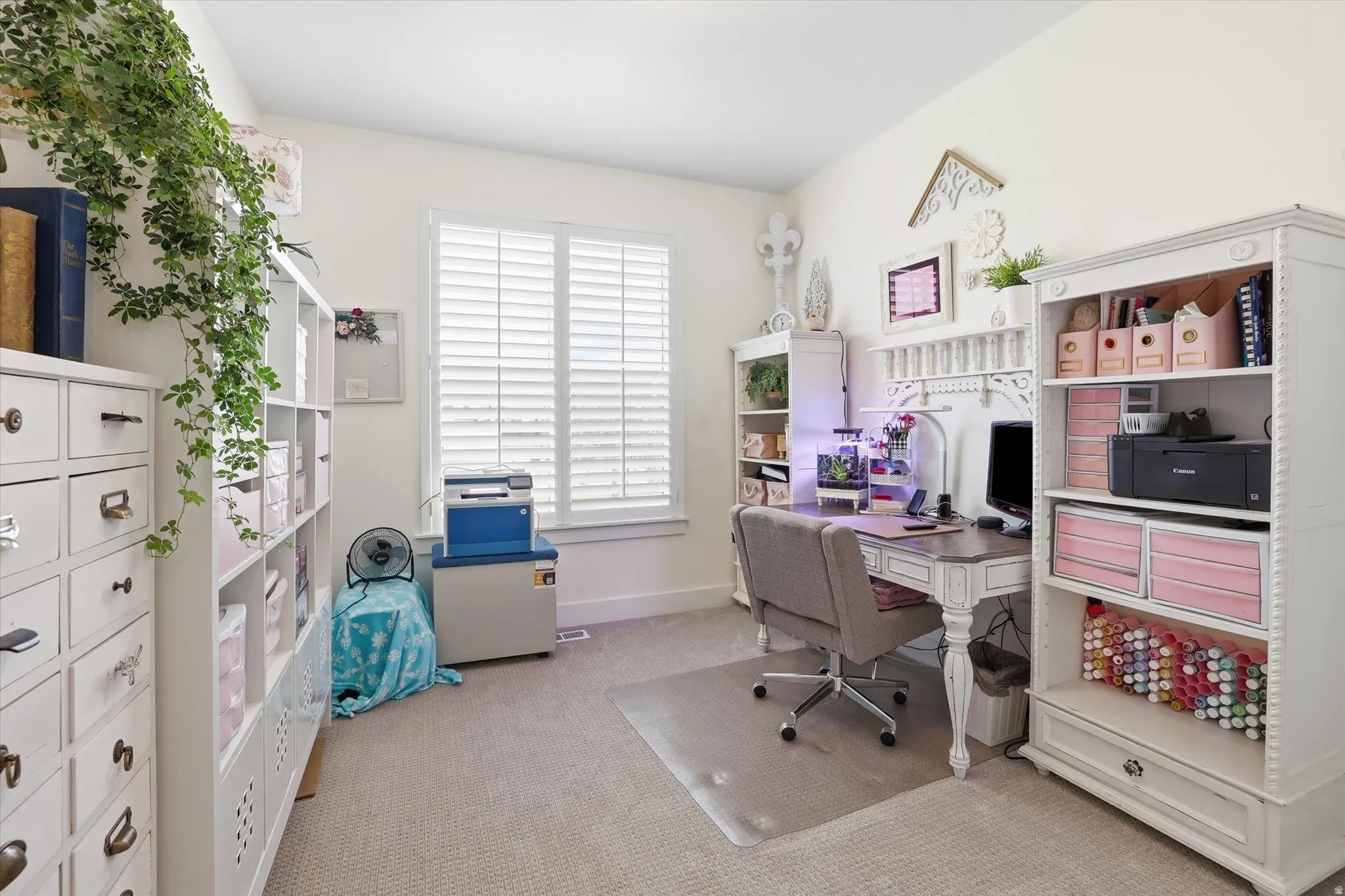 Bright room featuring a window with white plantation shutters, neutral carpeting, and white built-in shelving units