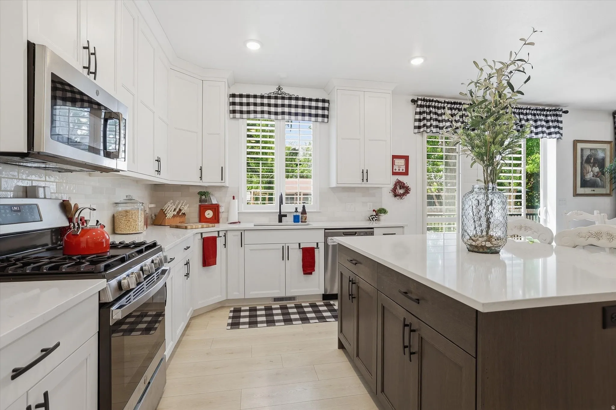 Modern kitchen featuring white shaker cabinetry, stainless steel appliances, a center island with a light-toned countertop, light wood-finish flooring, and a subway tile backsplash
