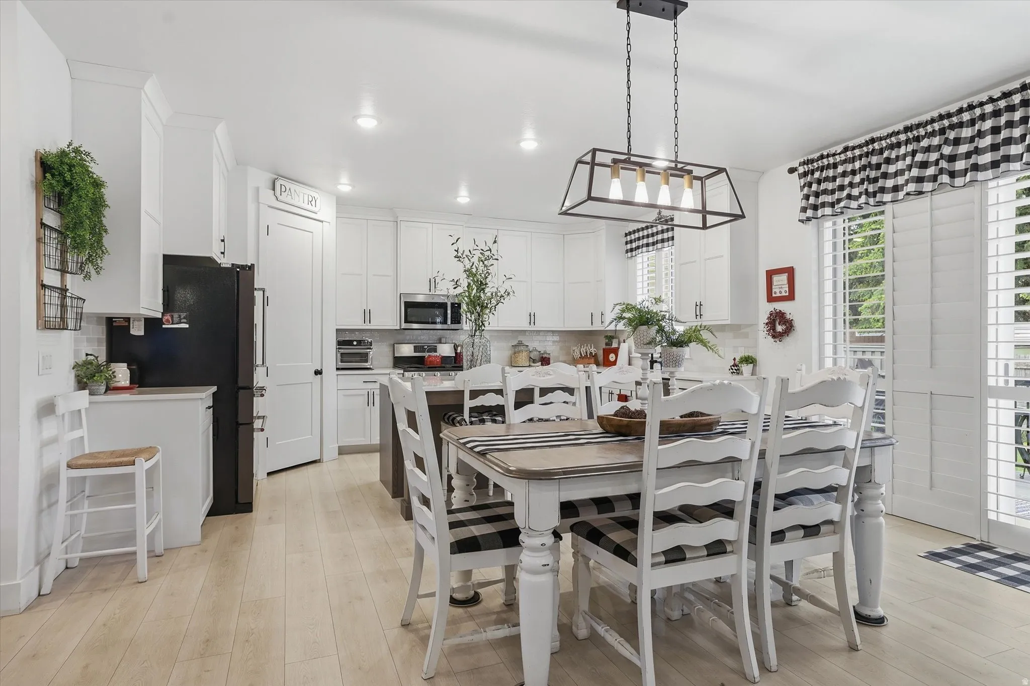 Bright kitchen featuring white cabinetry, light wood-finish flooring, a pantry door, a central island, and white plantation shutters