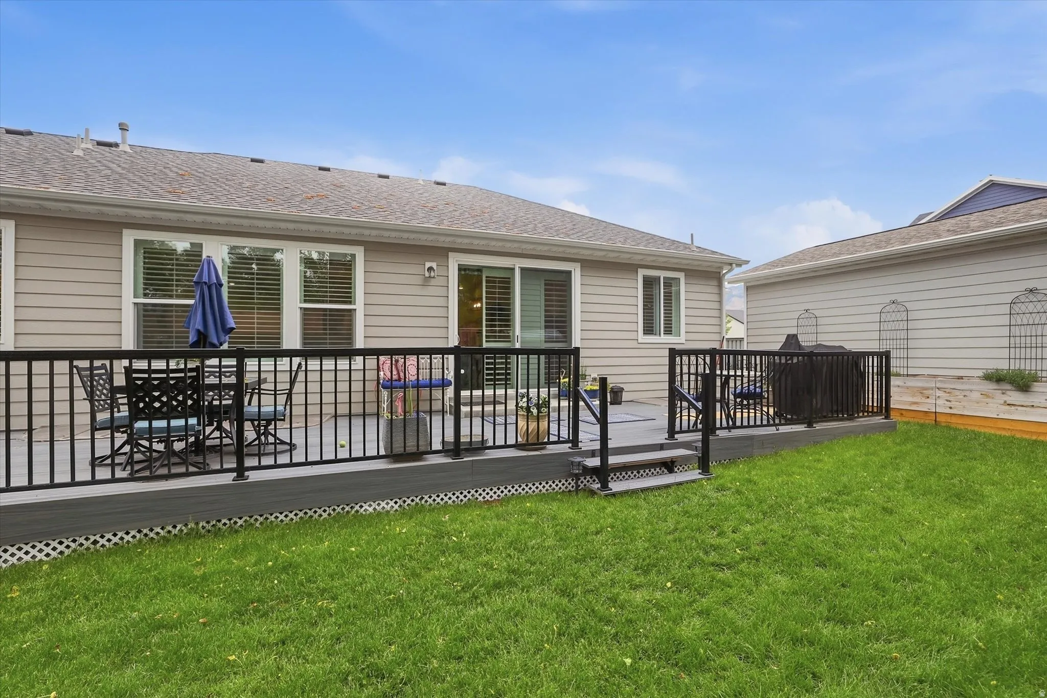 Rear exterior featuring a grey composite deck with black railings, a sliding glass door, multiple large windows with blinds, and a green lawn