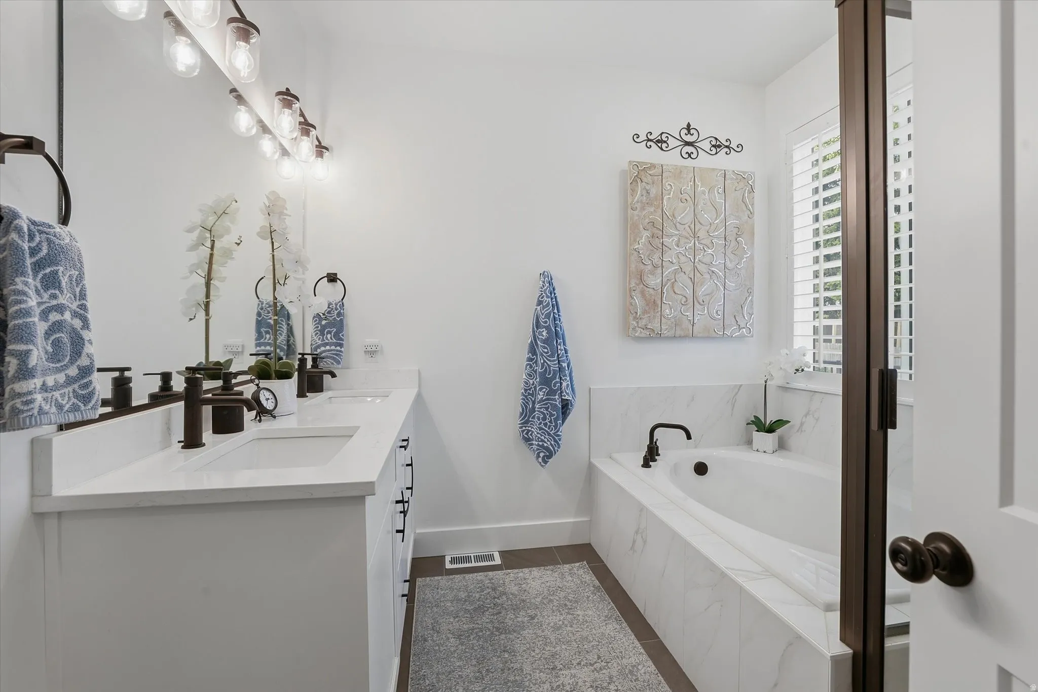 Bathroom featuring a double vanity with white cabinetry and quartz countertops, dual undermount sinks, and bronze-finish fixtures
