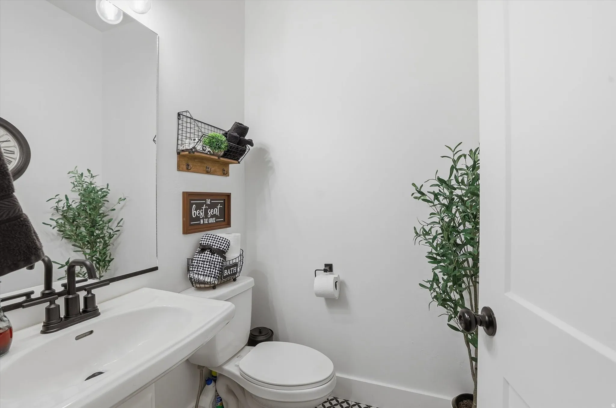 White pedestal sink with a matte black faucet, wall-mounted mirror, and overhead vanity lighting