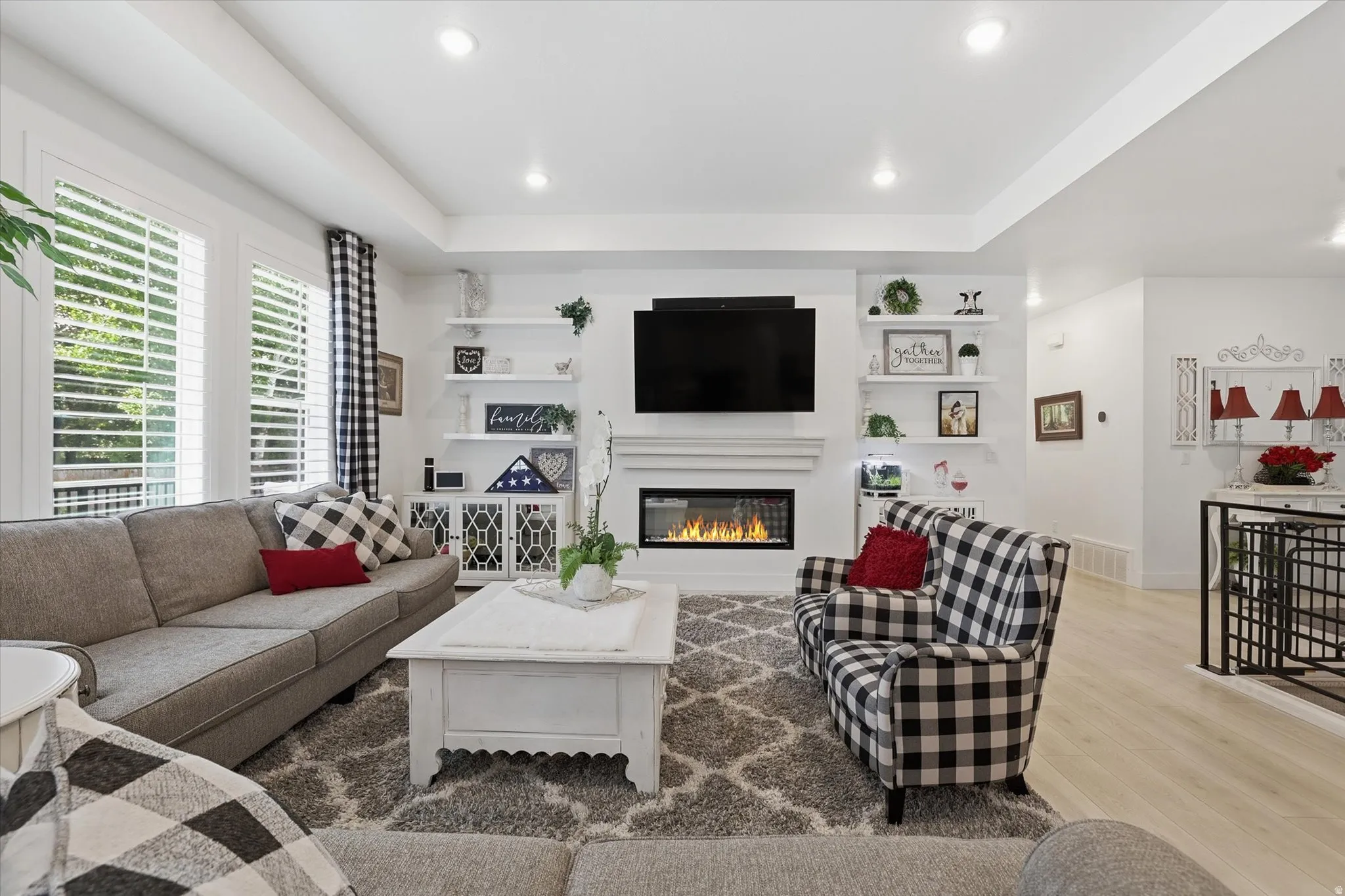 Living area featuring a modern fireplace with a white mantel, built-in shelving, recessed lighting, plantation shutters, and light wood-finish flooring