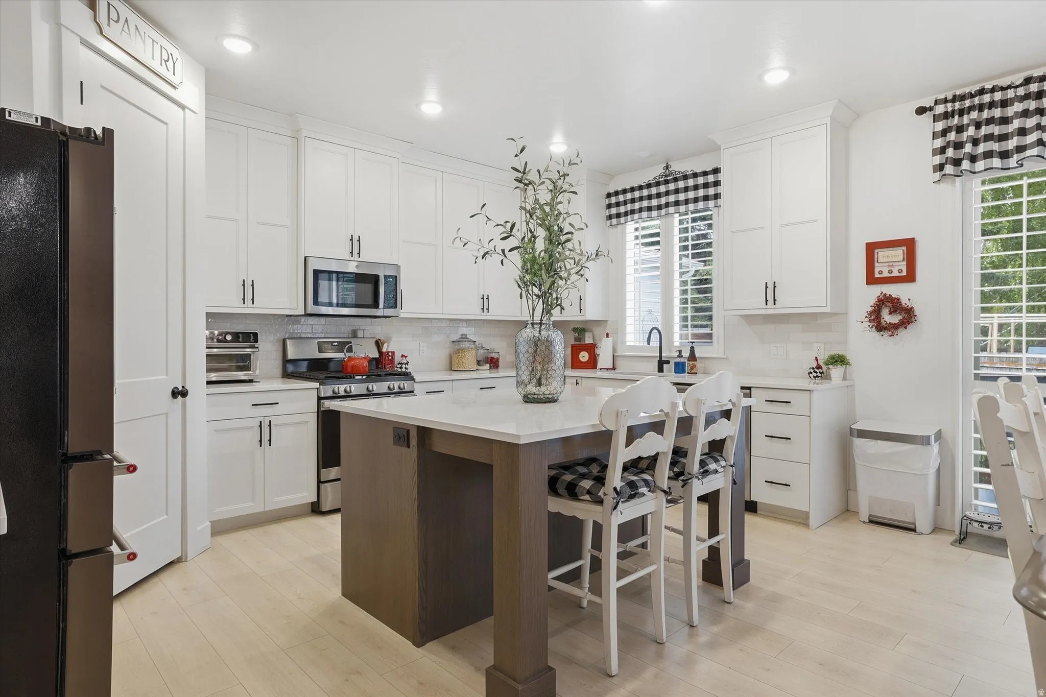 Kitchen featuring white shaker cabinetry, stainless steel appliances, a center island with bar seating, light wood-finish flooring, and a pantry door