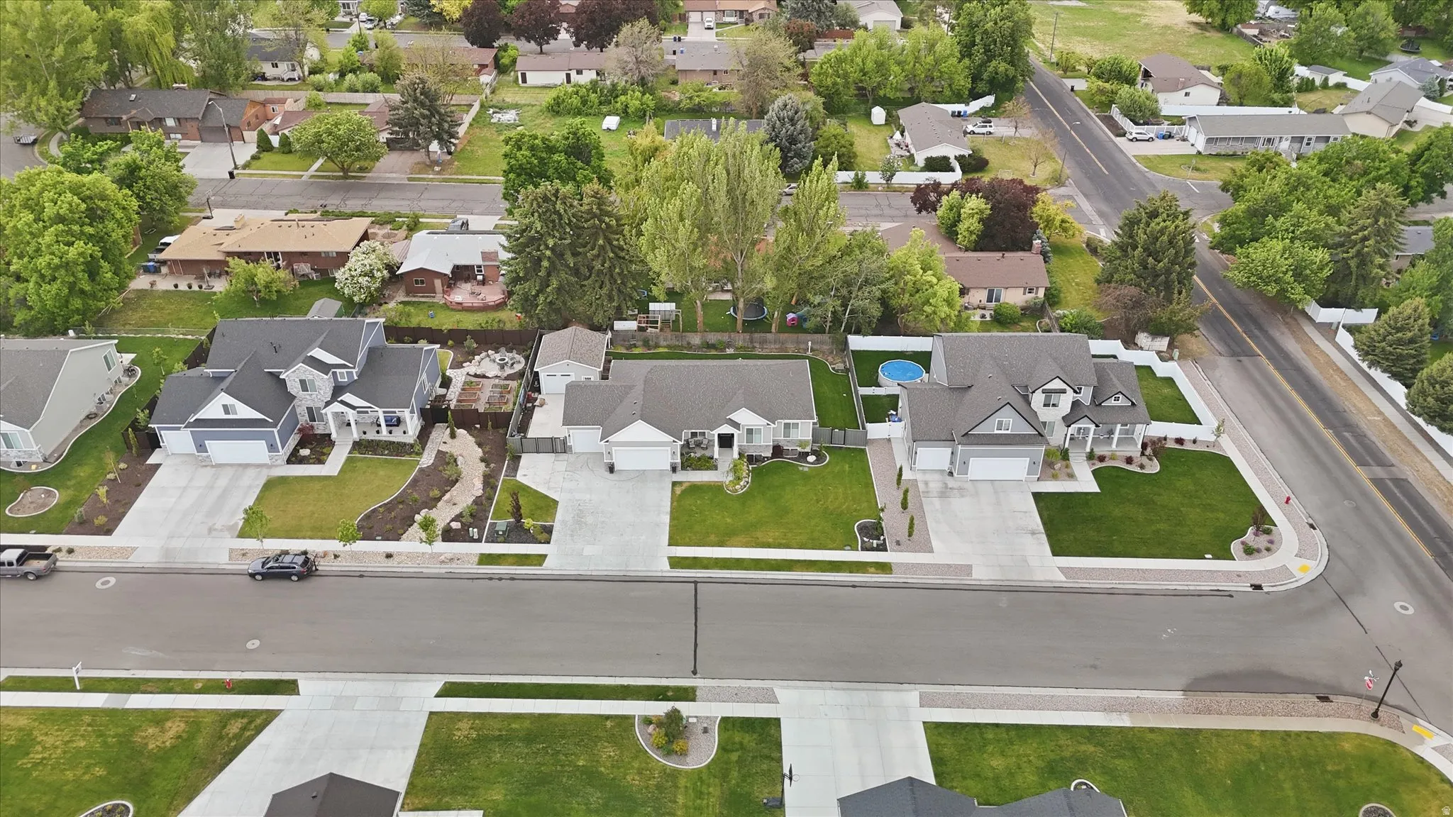 Residential street featuring three distinct homes with manicured lawns, concrete driveways, and surrounding green spaces