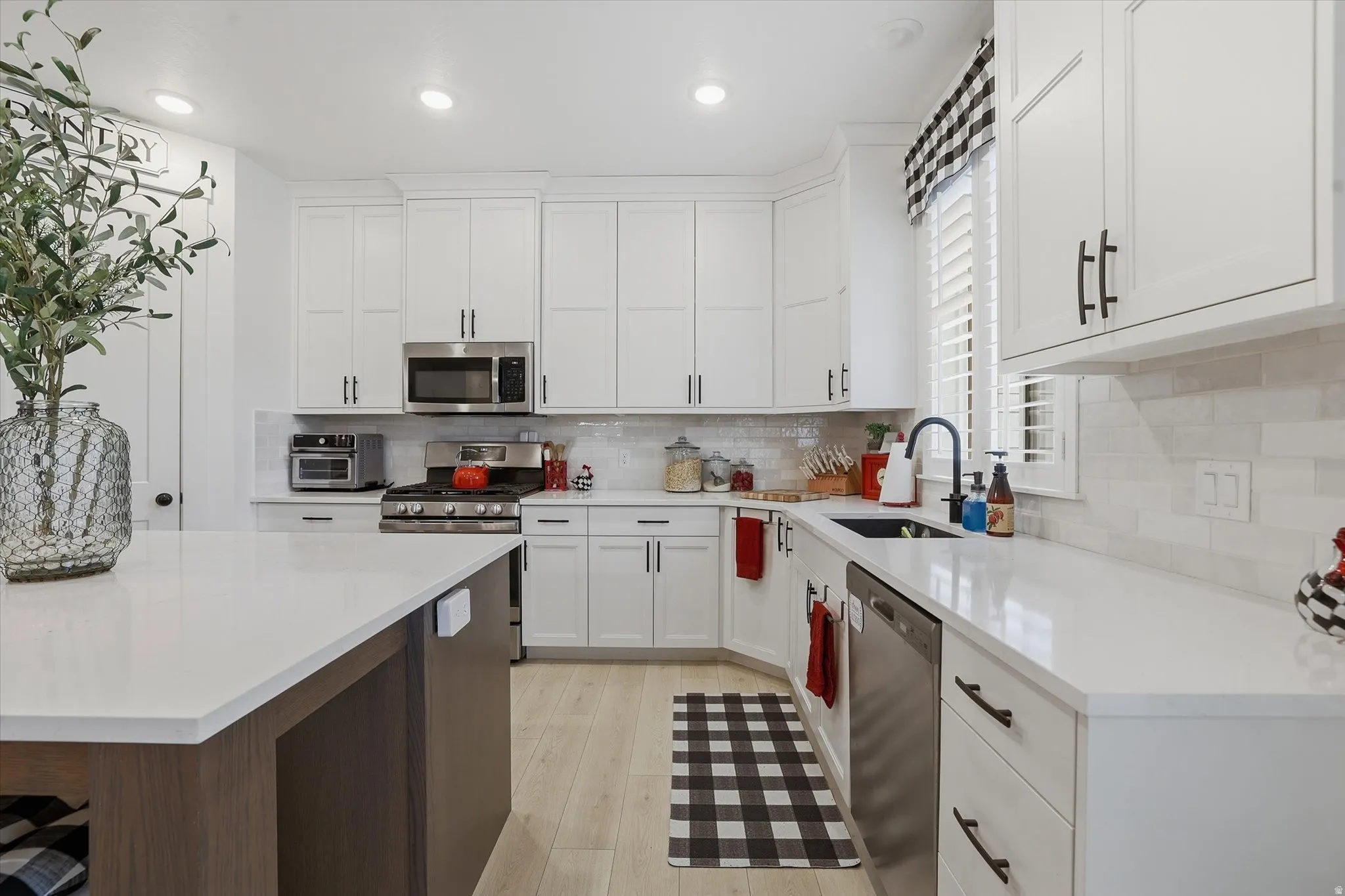 Kitchen featuring white shaker cabinetry, stainless steel appliances, a center island with a light countertop, white subway tile backsplash, and wood-finish flooring