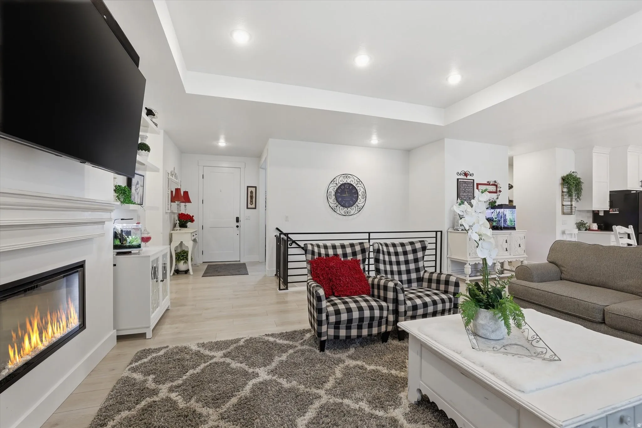 Open living space featuring a built-in electric fireplace with a white mantel, light wood-finish flooring, recessed lighting, and a partial view of a kitchen area