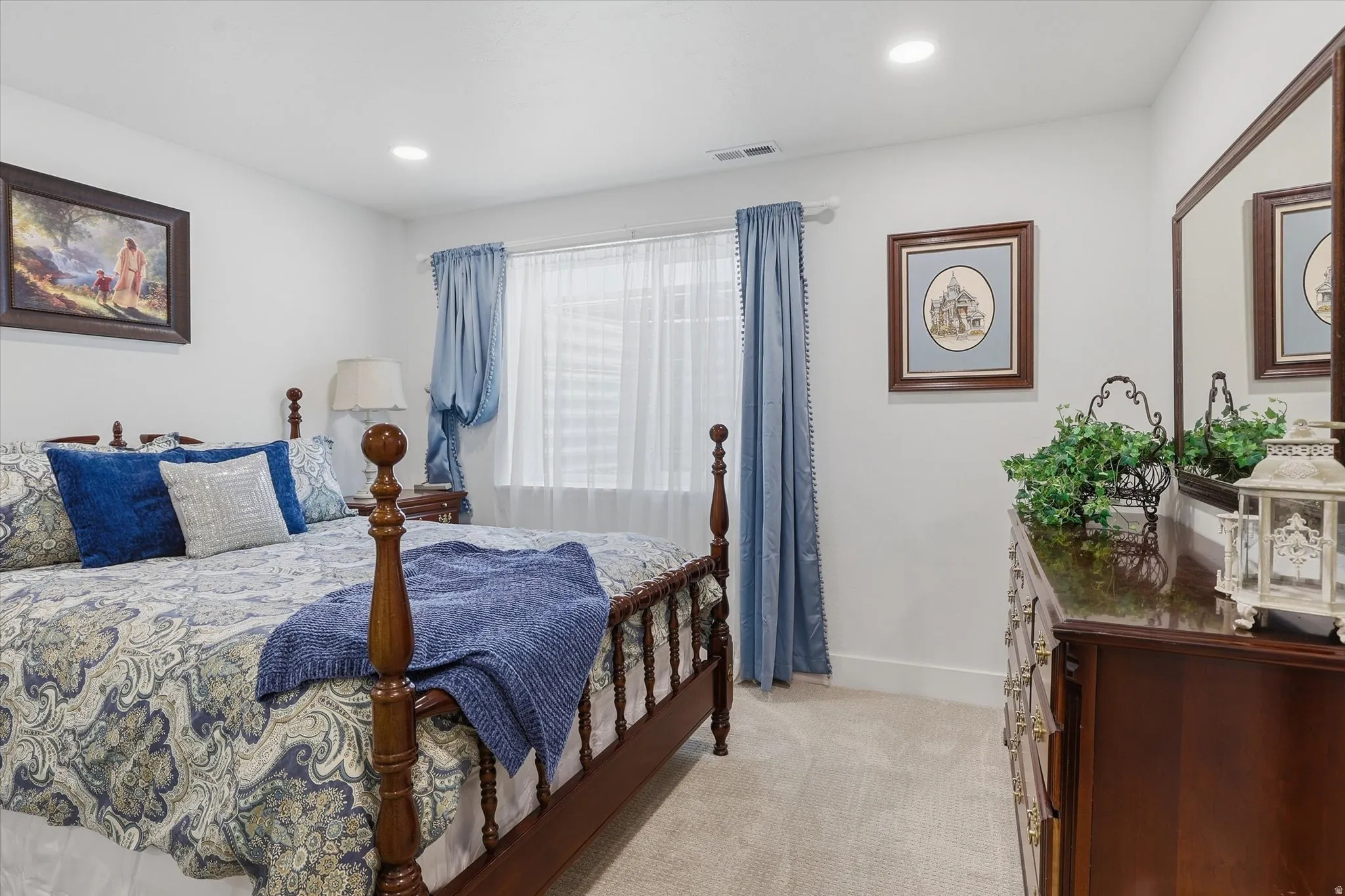 Carpeted bedroom featuring recessed lighting, a window with sheer and blue drapes, and a dark wood dresser with an attached mirror
