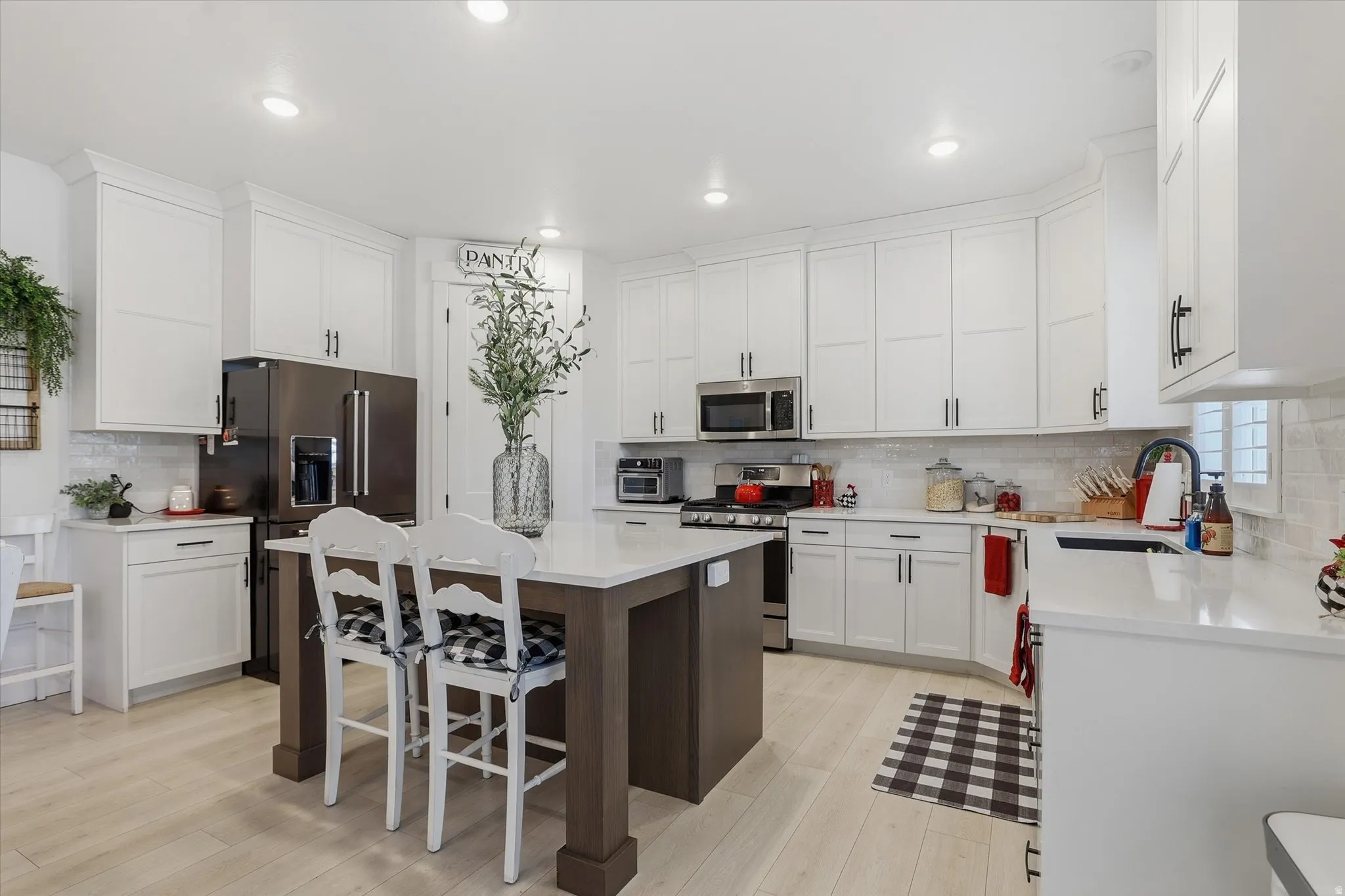 Bright kitchen featuring abundant white shaker cabinetry, light wood-finish flooring, a central island with countertop seating, stainless steel appliances, and a tiled backsplash