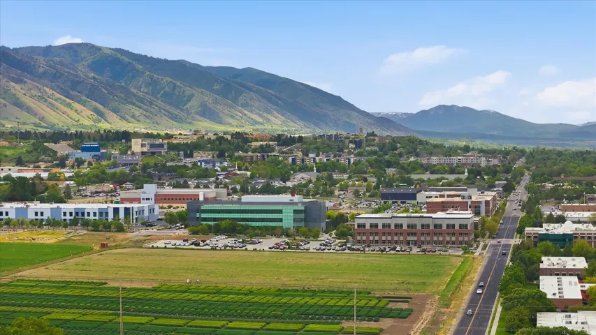 Expansive aerial perspective showcasing a mountainous backdrop, urban development, agricultural fields, and a multi-lane roadway