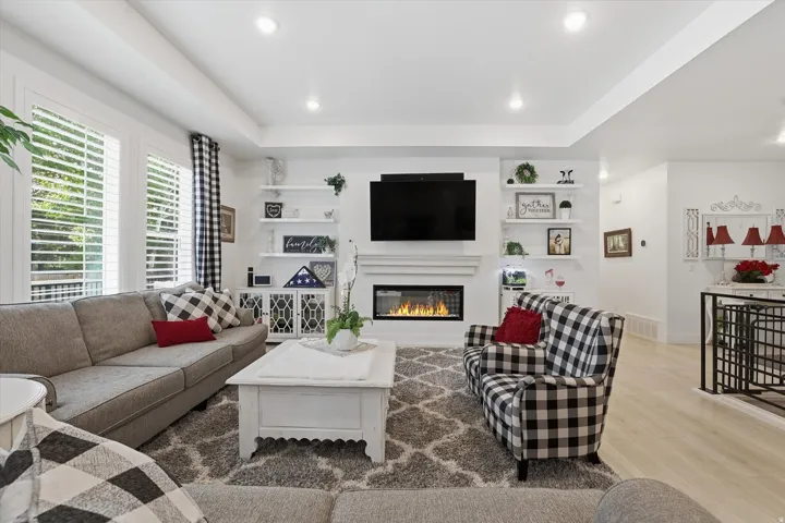 Living area featuring a modern fireplace with a white mantel, built-in shelving, recessed lighting, plantation shutters, and light wood-finish flooring