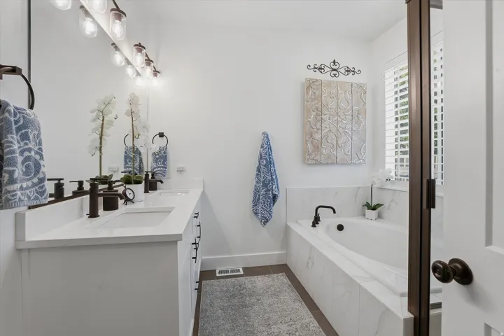 Bathroom featuring a double vanity with white cabinetry and quartz countertops, dual undermount sinks, and bronze-finish fixtures