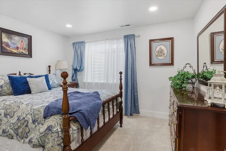Carpeted bedroom featuring recessed lighting, a window with sheer and blue drapes, and a dark wood dresser with an attached mirror